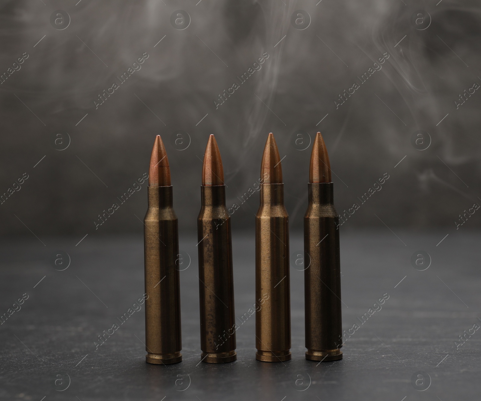 Firearm cartridges on grey table against smoke, closeup Photo of Firearm cartridges on grey table against smoke, closeup