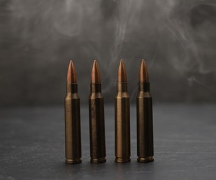 Photo of Firearm cartridges on grey table against smoke, closeup