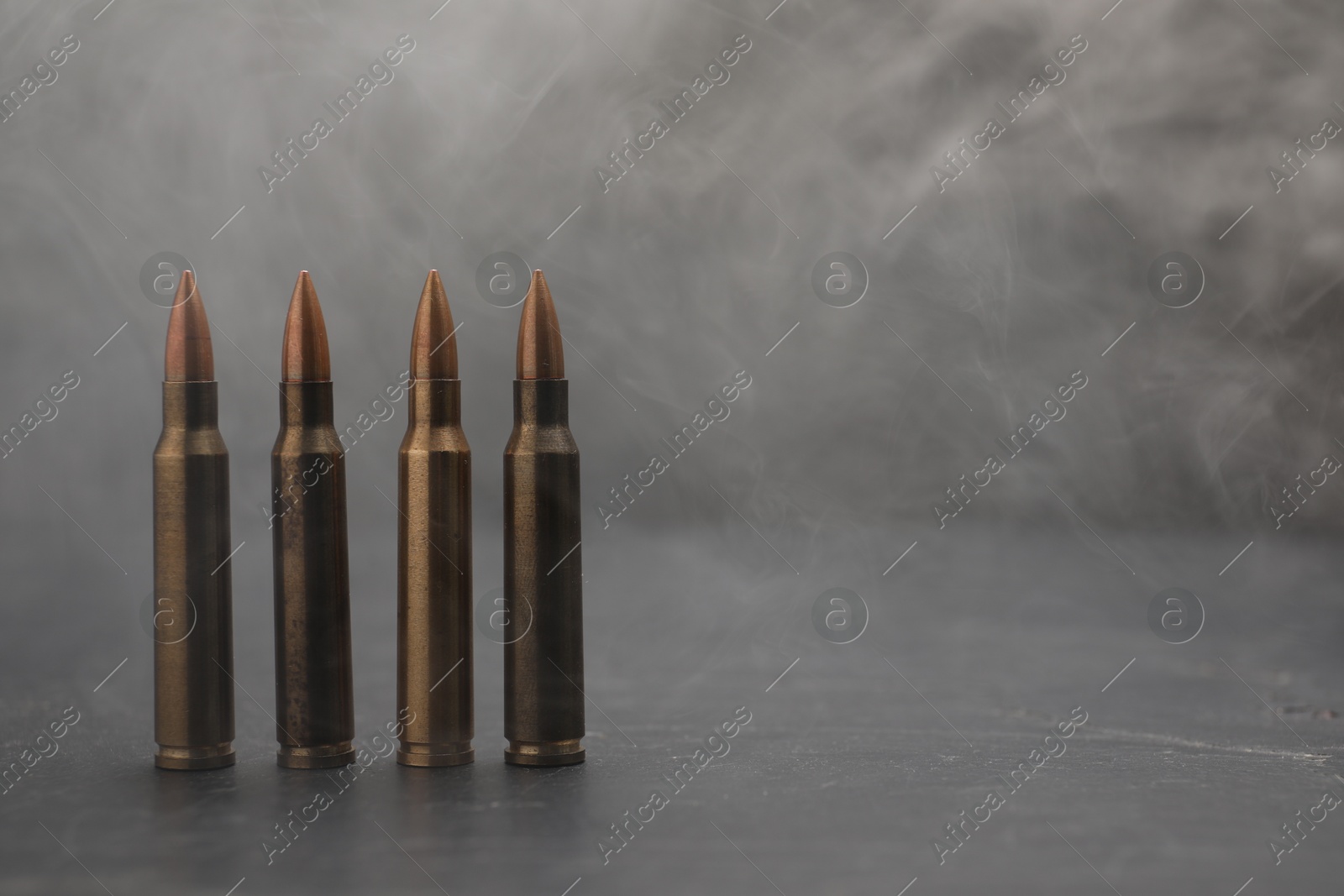 Firearm cartridges on grey table against smoke, closeup. Space for text Photo of Firearm cartridges on grey table against smoke, closeup. Space for text