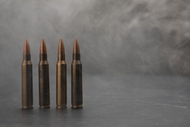 Photo of Firearm cartridges on grey table against smoke, closeup. Space for text
