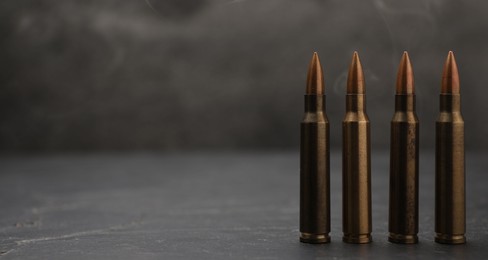 Photo of Firearm cartridges on grey table against smoke, closeup. Space for text