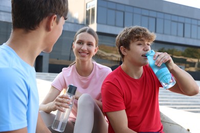 Photo of Group of teenagers with water bottles resting after training outdoors