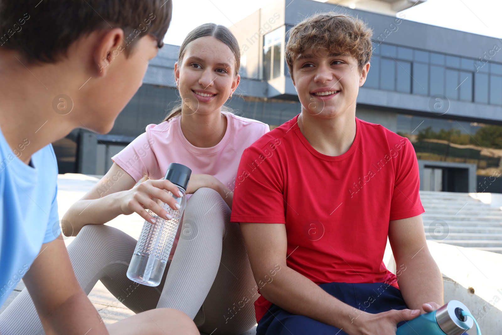 Group of teenagers with water bottles resting after training outdoors Photo of Group of teenagers with water bottles resting after training outdoors