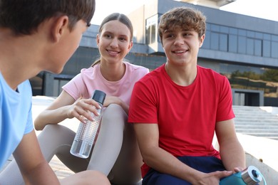 Photo of Group of teenagers with water bottles resting after training outdoors