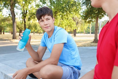 Photo of Teenage boy drinking water and talking to his friend after training outdoors