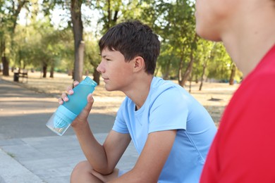 Photo of Teenage boy drinking water and talking to his friend after training outdoors