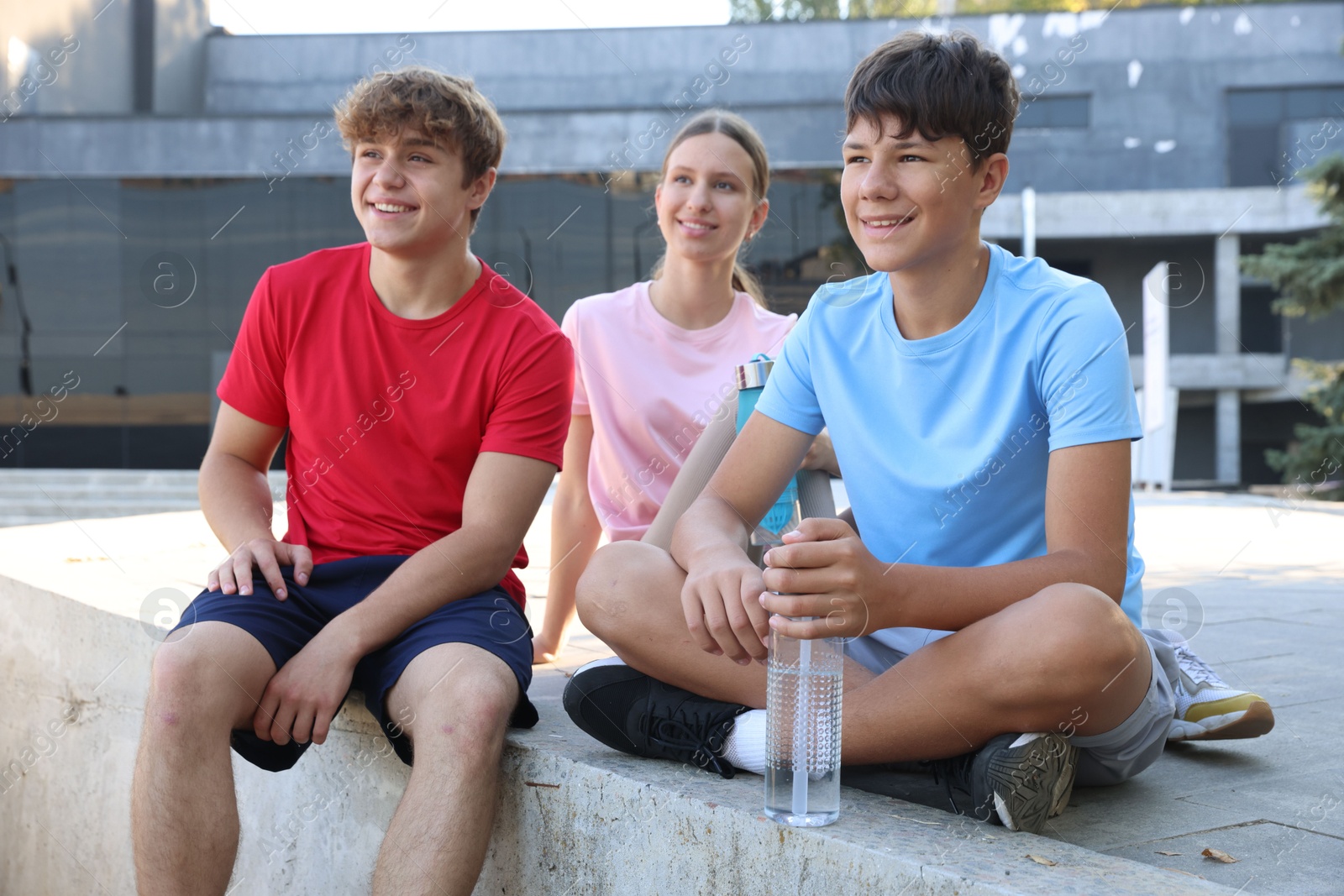 Group of teenagers with water bottles resting after training outdoors Photo of Group of teenagers with water bottles resting after training outdoors