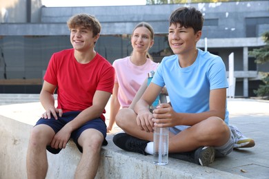 Photo of Group of teenagers with water bottles resting after training outdoors