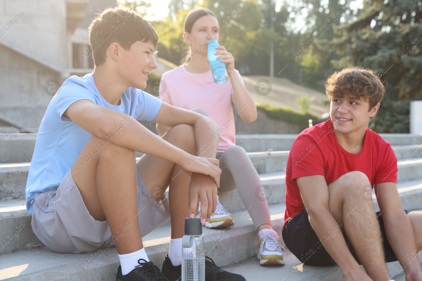 Group of teenagers with water bottles resting after training outdoors Photo of Group of teenagers with water bottles resting after training outdoors