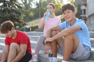 Photo of Group of teenagers with water bottles resting after training outdoors