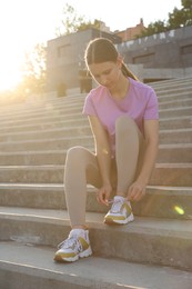 Photo of Teenage girl tying shoelaces before running on stairs outdoors