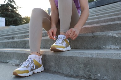 Photo of Teenage girl tying shoelaces before running on stairs outdoors, closeup