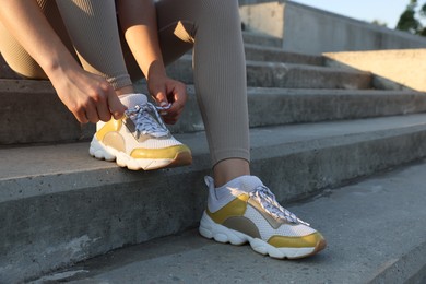 Photo of Teenage girl tying shoelaces before running on stairs outdoors, closeup