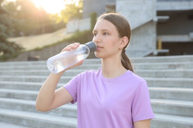 Photo of Teenage girl drinking water during training outdoors