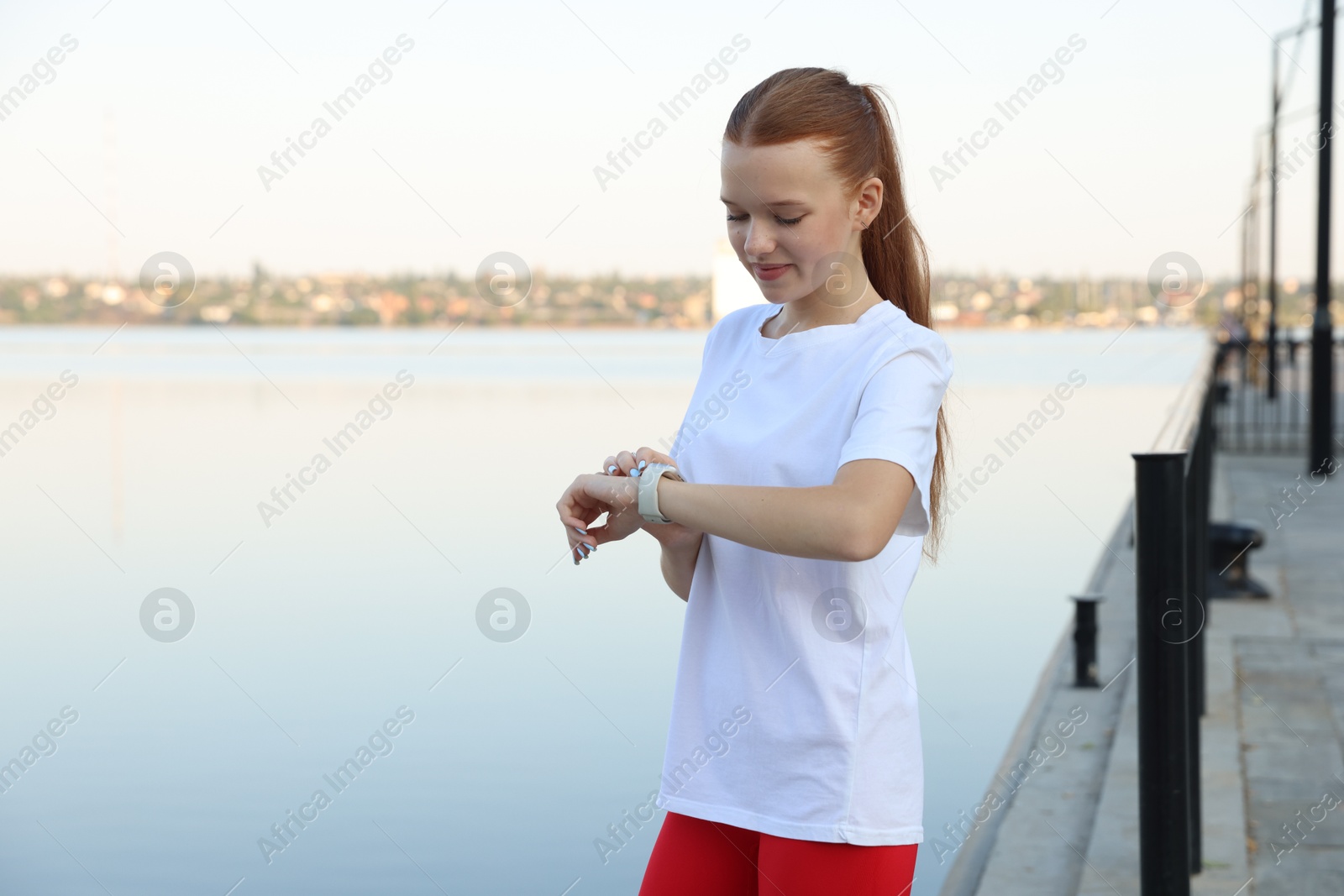 Teenage girl checking pulse via watch after training outdoors. Space for text Photo of Teenage girl checking pulse via watch after training outdoors. Space for text