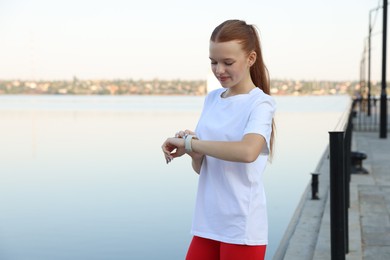 Photo of Teenage girl checking pulse via watch after training outdoors. Space for text