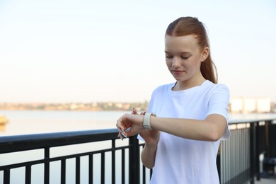Photo of Teenage girl checking pulse via watch after training outdoors. Space for text