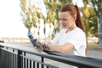 Photo of Teenage girl with water bottle checking pulse via watch after training outdoors