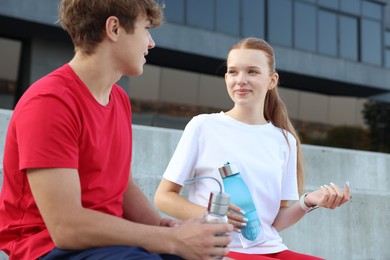 Photo of Teenage boy and girl with water bottles after training outdoors