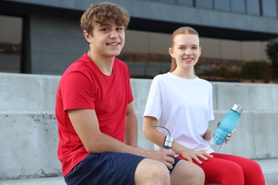 Photo of Teenage boy and girl with water bottles after training outdoors