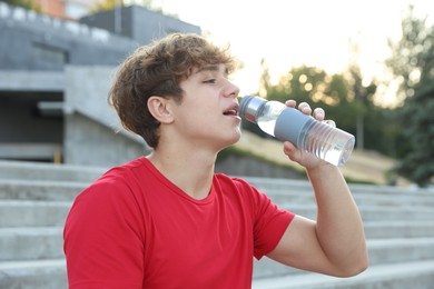 Photo of Teenage boy drinking water after training outdoors