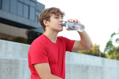 Photo of Teenage boy drinking water after training outdoors