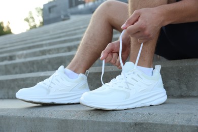 Photo of Teenage boy tying shoelaces before running on stairs outdoors, closeup