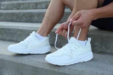 Photo of Teenage boy tying shoelaces before running on stairs outdoors, closeup
