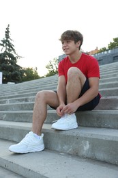 Photo of Teenage boy tying shoelaces before running on stairs outdoors