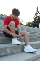 Photo of Teenage boy tying shoelaces before running on stairs outdoors