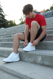 Photo of Teenage boy tying shoelaces before running on stairs outdoors