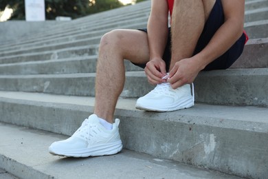 Photo of Teenage boy tying shoelaces before running on stairs outdoors, closeup