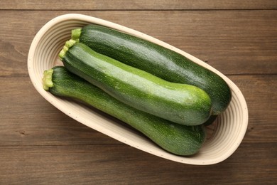 Photo of Fresh ripe zucchinis in wicker basket on wooden table, top view