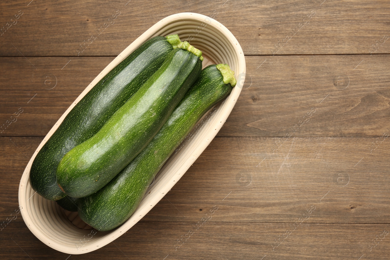Fresh ripe zucchinis in wicker basket on wooden table, top view. Space for text Photo of Fresh ripe zucchinis in wicker basket on wooden table, top view. Space for text
