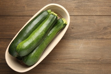Photo of Fresh ripe zucchinis in wicker basket on wooden table, top view. Space for text