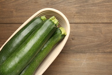 Photo of Fresh ripe zucchinis in wicker basket on wooden table, top view. Space for text
