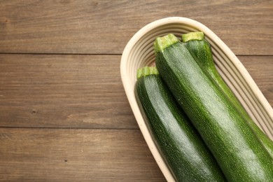 Photo of Fresh ripe zucchinis in wicker basket on wooden table, top view. Space for text