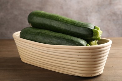 Photo of Fresh ripe zucchinis in wicker basket on wooden table, closeup