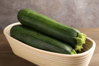 Photo of Fresh ripe zucchinis in wicker basket on wooden table, closeup