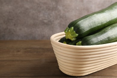 Photo of Fresh ripe zucchinis in wicker basket on wooden table, closeup. Space for text