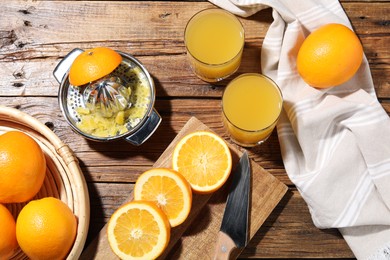 Photo of Freshly squeezed orange juice, fruits and juicer on wooden table, flat lay