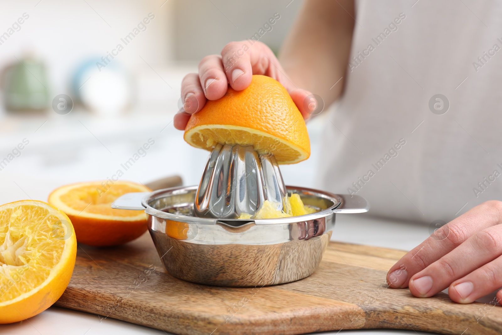 Making juice. Woman with orange using juicer at table indoors, closeup Photo of Making juice. Woman with orange using juicer at table indoors, closeup