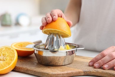 Photo of Making juice. Woman with orange using juicer at table indoors, closeup