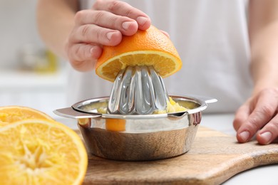 Photo of Making juice. Woman with orange using juicer at table indoors, closeup
