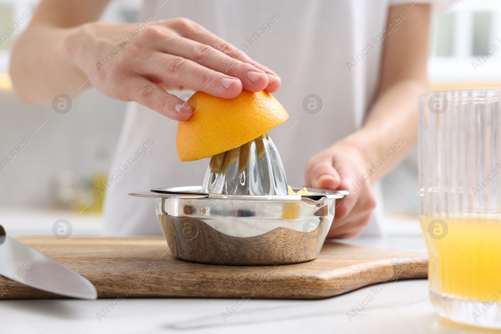 Making juice. Woman with orange using juicer at white marble table indoors, closeup Photo of Making juice. Woman with orange using juicer at white marble table indoors, closeup