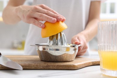 Photo of Making juice. Woman with orange using juicer at white marble table indoors, closeup