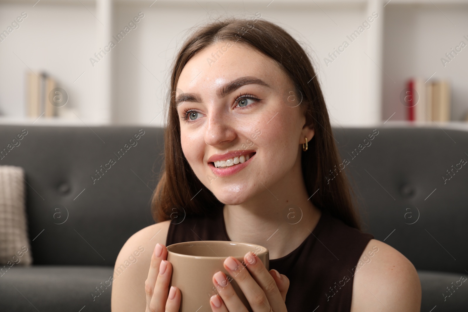 Photo of Beautiful woman with cup of drink near sofa at home