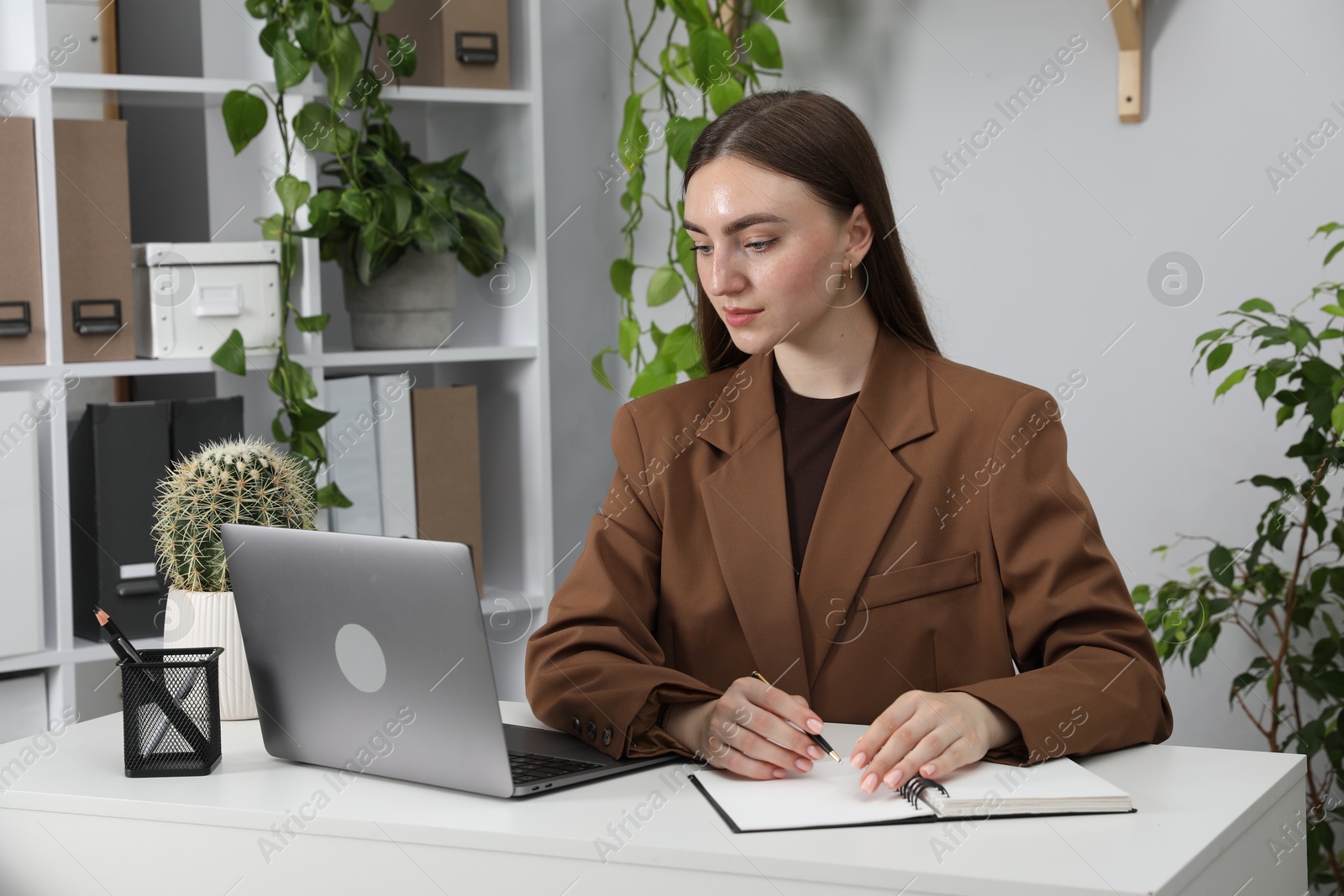 Photo of Woman taking notes while working with laptop at desk in office