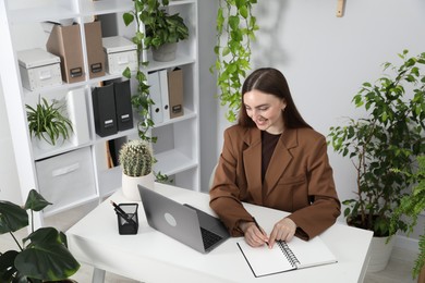 Photo of Woman taking notes while working with laptop at desk in office, above view