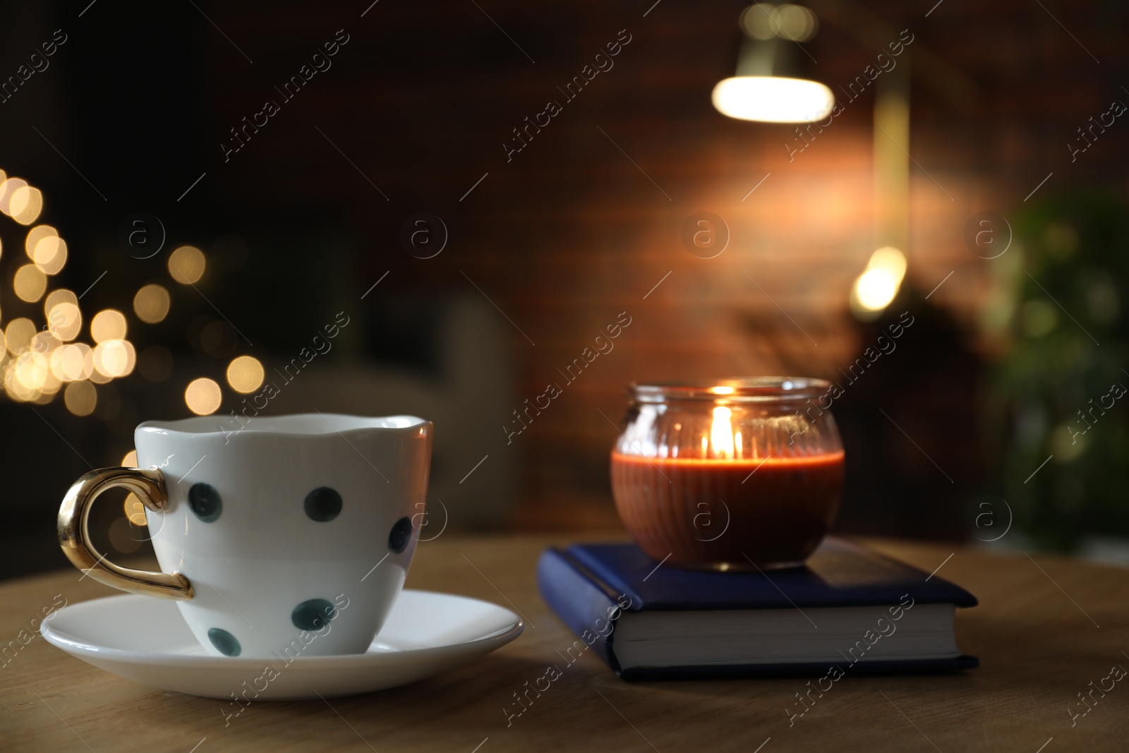 Cup of tea, burning candle and book on wooden table against blurred lights, closeup Photo of Cup of tea, burning candle and book on wooden table against blurred lights, closeup
